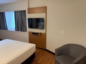 a bedroom with a bed and a chair and a television at Flat Particular no Comfort Suites in Brasilia