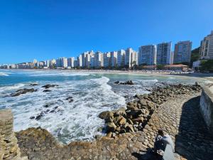 a person sitting on a rocky beach near the ocean at Frente Mar! Apartamento TOP, experiência única! in Guarujá