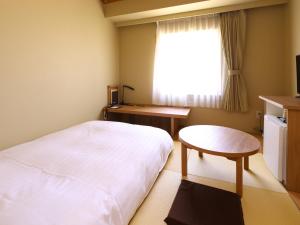 a bedroom with a bed and a table and a window at Dormy Inn Express Mikawaanjo in Anjomachi