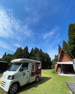 una furgoneta blanca y roja estacionada en un campo en Guesthouse Coco Garage, en Kirishima