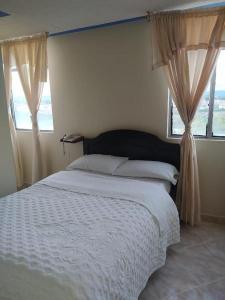 um quarto com uma cama branca e 2 janelas em Hotel Noche Bella em Ipiales