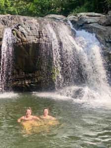 deux garçons nageant dans l'eau devant une cascade dans l'établissement Thomasha Homestay & Tuk Tuk Service, à Wellawaya