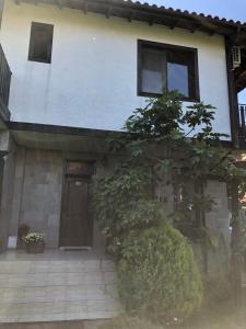 辛尼莫雷特Вила Стела的白色的房子,有一扇门和一些灌木丛