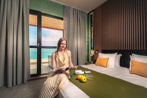 a woman sitting on a bed in a hotel room at Hotel Palms Beach Kiten in Kiten