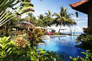 un complejo con piscina con palmeras y el océano en Teluk Karang Dive & Spa Resort, en Tejakula