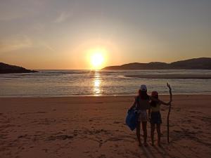 dos mujeres de pie en la playa al atardecer en Casa Jesús Turismo Rural en Lires