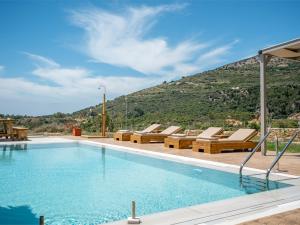a pool with lounge chairs and a mountain in the background at Pantheon Luxury Villas in Skala