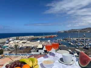 - une table avec des fruits et des verres à vin et une vue sur le port dans l'établissement SUNNY DAY Deluxe 1, à Arguineguín