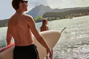 mężczyzna i kobieta trzymający deskę surfingową w wodzie w obiekcie HERMITAGE Lake Lucerne - Beach Club & Lifestyle Hotel w Lucernie