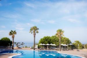 uma piscina com palmeiras e guarda-sóis em Pomegranate Wellness Spa Hotel em Nea Potidaea