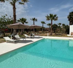 a swimming pool with chairs and umbrellas and palm trees at B&B Brezza Delle Egadi in Marsala