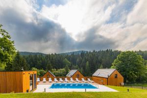 a large swimming pool with chairs in front of wooden buildings at Gwiazda Mogielicy basen & balia, sauna in Słopnice
