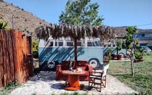 un tavolo e sedie sotto un ombrellone accanto a un furgone di Cornelia Hippie Magic Bus a Kíssamos