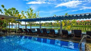 a resort pool with chairs and a view of the water at Riverside White House Boutique Hotel in Hoi An