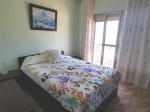 a bedroom with a bed with a flowered blanket and a window at Casa Corales in Castell de Ferro