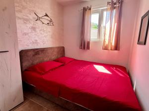 - un lit rouge dans une petite chambre avec fenêtre dans l'établissement Apartments Obradovic, à Krasići