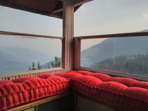 um sofá vermelho sentado numa sala com duas janelas em THE WONDERLAND COTTAGES & Cafe em Narkanda