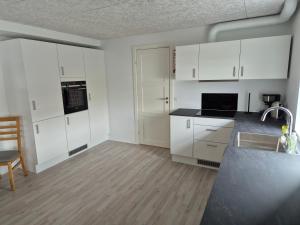 an empty kitchen with white cabinets and a sink at Cosy apartment in Norðskála in Norðskáli