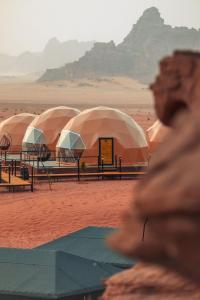 Faisal Wadi Rum camp في وادي رم: صف من القباب في صحراء مع جبال في الخلفية