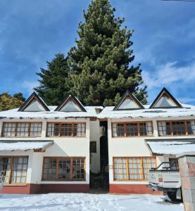 a house with a pine tree in the snow at LA PONDEROSA Apart Hotel in San Carlos de Bariloche