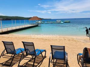 a group of chairs on a beach with a dock at VaeTropicalParadise Free Beach & Pool Access in Discovery Bay