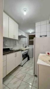 une cuisine avec des armoires blanches et un réfrigérateur dans l'établissement Apartamento super aconchegante a 250 mts da Praia, à Guarapari