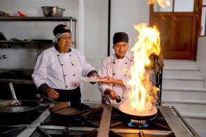 two chefs standing in a kitchen with a stove with fire at Quechua Hotel Cusco in Cusco