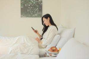 uma mulher sentada numa cama a olhar para um telemóvel em Aank Hotel Incheon Wolgot em Siheung