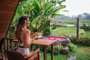a woman sitting at a table with a cup of coffee at Tri Dewi Residence by Pramana Villas in Ubud