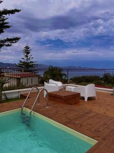 a pool with white chairs and a table and a wooden deck at Panorama del golfo in Balestrate