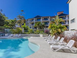 a row of white lounge chairs next to a swimming pool at Bella Mare Coolangatta Beachside Apartments in Gold Coast