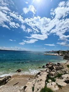 a beach with rocks and a blue sky and clouds at Accordi Lontani in Nerezine