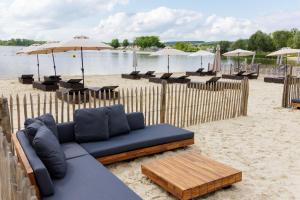 a couch on the beach with tables and umbrellas at Center Parcs Le Lac d’Ailette in Chamouille