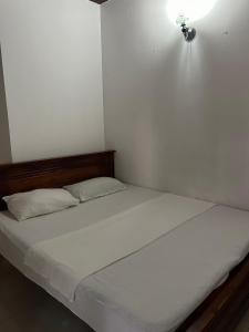Himo Guest Inn في دهيفالا: سرير بملاءات بيضاء واضاءة على الحائط