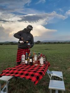 sunshine maasai Mara safari camp in Kenya في Sekenani: رجل يقف بجوار طاولة نزهة مع زجاجات من الكحول