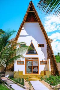 a house with a thatched roof on a beach at La Perla Beach Resort, Zanzibar - Your Beachfront Private Haven in Pwani Mchangani