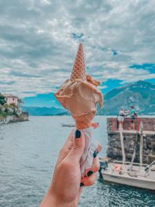 une main tenant un cône de crème glacée devant l'eau dans l'établissement Ostello Bello Lake Como, à Côme
