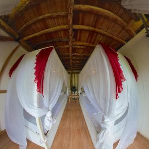 1 dormitorio con cortinas blancas y rojas y techo de madera en De Chicktoria Hostel en Pawenang
