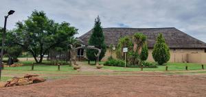 a house with a large roof with trees in front of it at Tava Lingwe Game Lodge & Wedding Venue in Parys