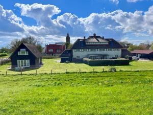 une grande maison blanche dans un champ d'herbe verte dans l'établissement Villa Nieuwland holiday home, à Den Oever