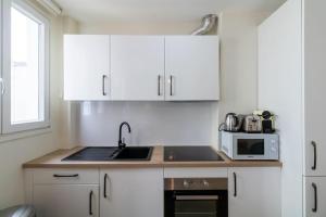 Una cocina con gabinetes blancos, un fregadero y un microondas. en B3#Two Bedrooms#Champs Elysées#Arc de Triomphe#AC, en París