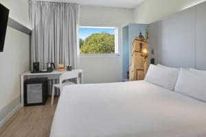 a bedroom with a white bed and a desk and a window at B&B HOTEL Barcelona Granollers in Les Franqueses del Vallès