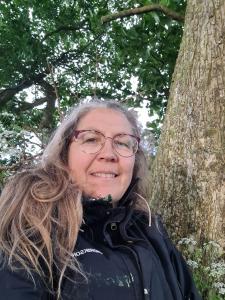 a woman wearing glasses standing next to a tree at Naturlig Viis in Øster Ulslev