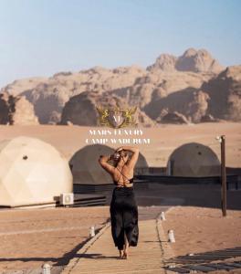 a woman walking down a road in the desert at MARS LUXURY CAMP WADi RUM in Wadi Rum