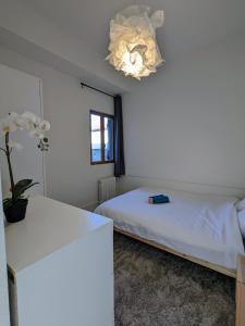 a white bedroom with a bed and a chandelier at La pause roannaise in Roanne +7 photos