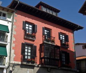 czerwony budynek z czarnymi oknami i balkonami w obiekcie Hotel Palacio Oxangoiti w mieście Lekeitio