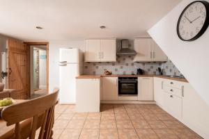 a kitchen with white cabinets and a clock on the wall at The Byre, Heritage Escapes, Field House Farm in Bempton