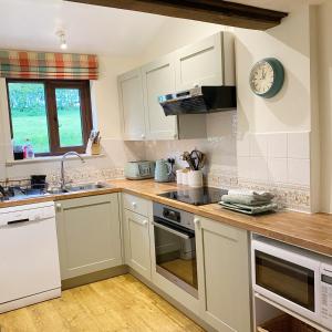 a kitchen with white cabinets and a clock on the wall at Llynhillyn Cottage in Presteigne