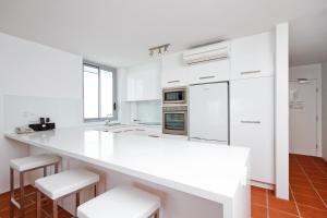 a white kitchen with white appliances and white stools at Fairshore 38 Beachfront Balcony in Noosa Heads