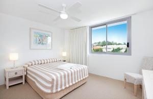 a white bedroom with a bed and a window at Fairshore 38 Beachfront Balcony in Noosa Heads +5 photos